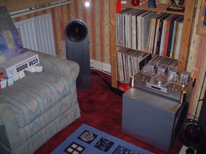 Photograph: a silver subwoofer box in the room, with a valve CD player on top, and a Transparence in the background