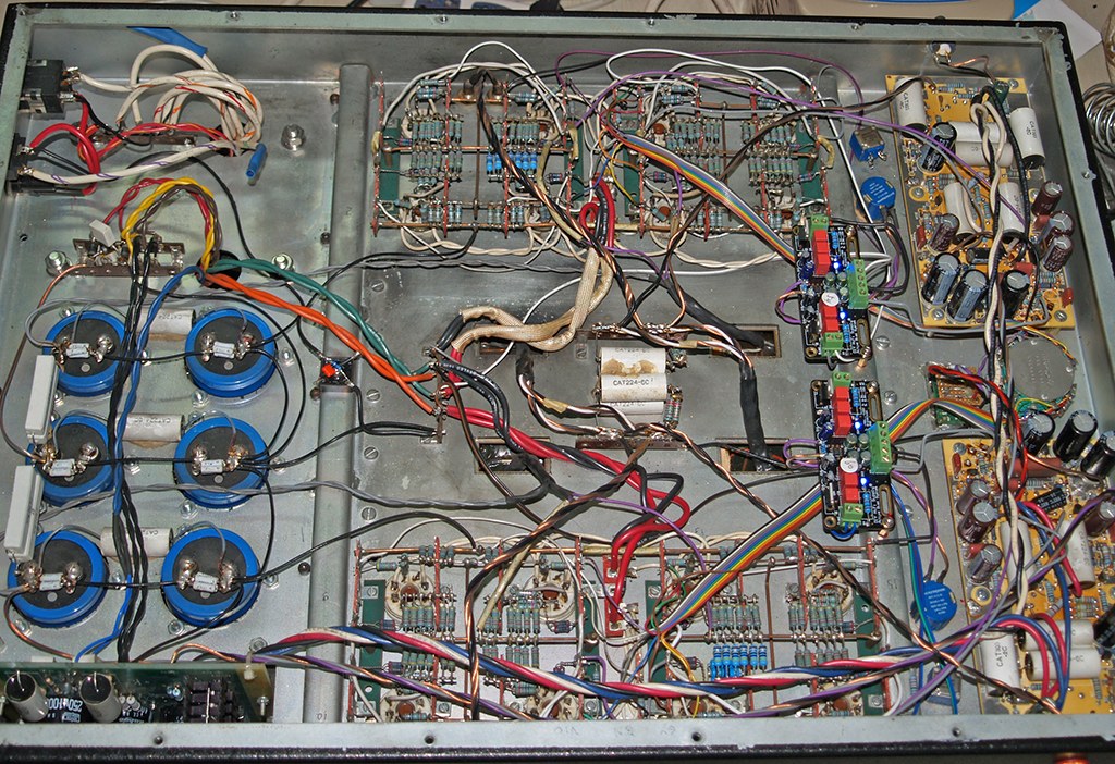 Photograph: the underside of the amplifier chassis, showing point-to-point wiring, circuit boards and a bank of large blue capacitors